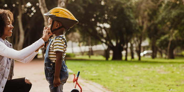 Mom helps her son put on a helmet so he can ride his bike safely